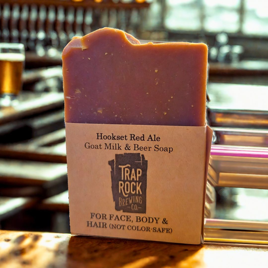 Bar of soap with packaging labeled 'Hookset Red Ale Goat Milk & Beer Soap' from Trap Rock Brewing Co. on a wooden surface.